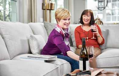 two women enjoy a glass of wine on couch
