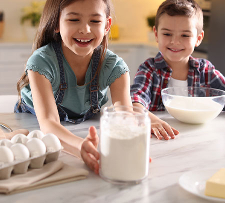 two children with cooking ingredients on a granite countertop