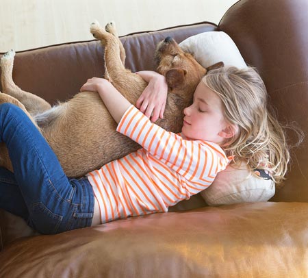 girl and dog laying on leather couch